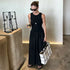 Woman in a black dress holding a white tote bag and a drink, standing in a modern indoor setting.